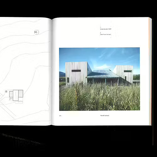 An open architectural design book or magazine spread, showing a printed photograph of a modern building with tall grass in the foreground on the right page, alongside minimalist line drawings on the left page, photographed against a black background.