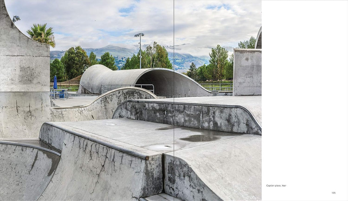 A wide-angle photograph of a concrete skatepark with curved ramps and a tunnel-like bowl, set against a backdrop of trees, distant mountains, and a cloudy sky. The photo is presented as a double-page spread with a white margin on the right side.