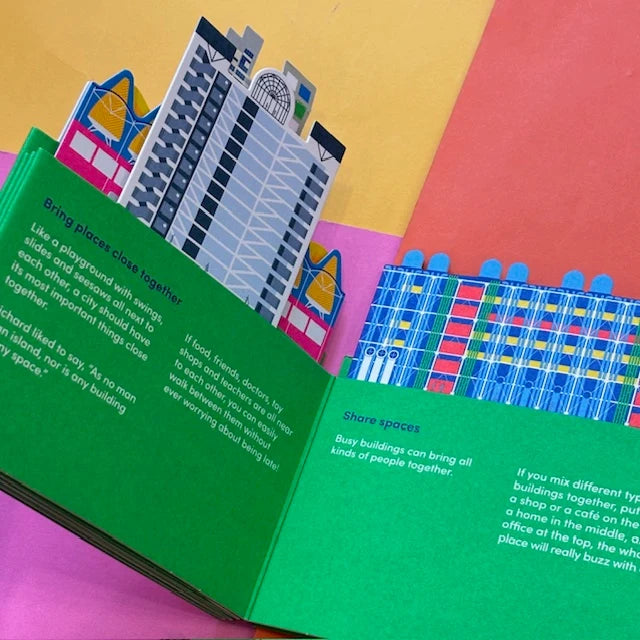 An open children's pop-up book with colorful cityscape pop-ups, photographed on a bright multicolor paper background.