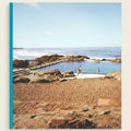 Natural rock pool with people around, surrounded by sandy beach and ocean.