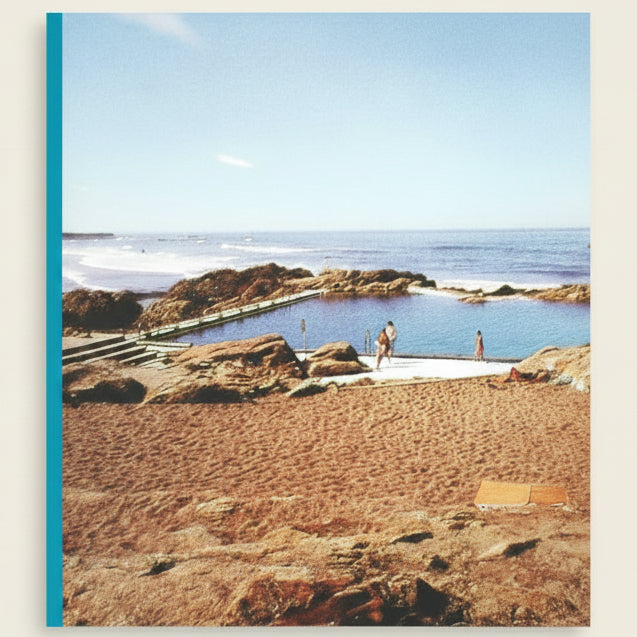Natural rock pool with people around, surrounded by sandy beach and ocean.
