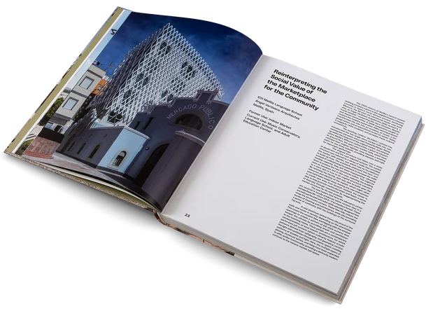 An open hardcover book photographed on a clean white background. The left page shows a large architectural photograph with a dark blue sky and a modern building facade; the right page contains columns of text under a headline.