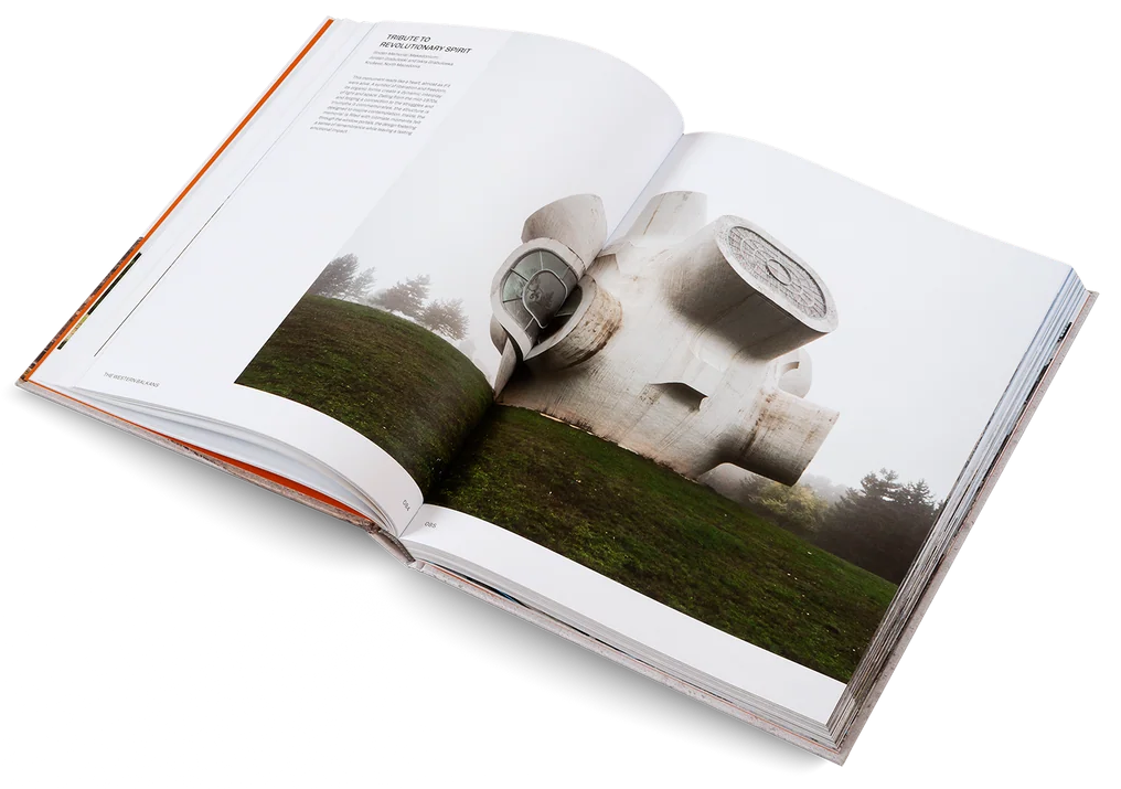 An open hardcover book photographed on a clean white background, showing a large architectural photograph on the spread with a white structure over green grass.
