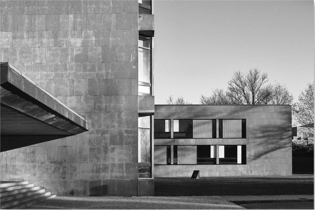 Black and white architectural photograph of a modernist concrete building with geometric forms, strong shadows, and bare trees in the background.