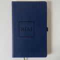 Navy blue notebook with 'Riai' embossed on the cover against a light gray background