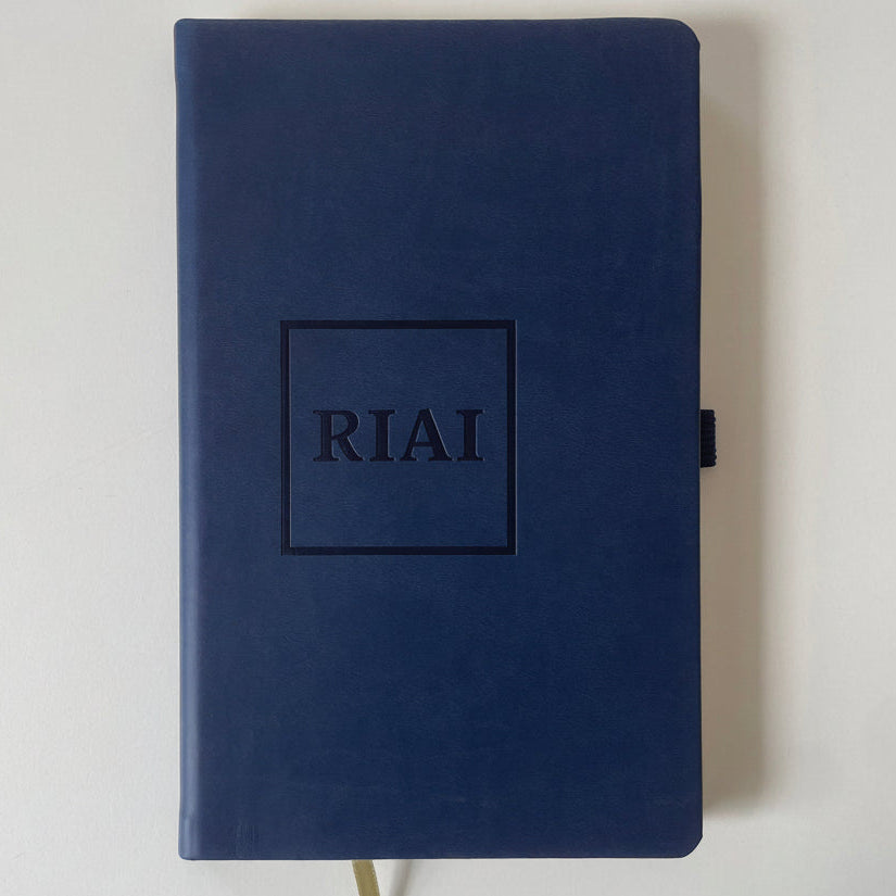 Navy blue notebook with 'Riai' embossed on the cover against a light gray background