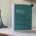 Spiral-bound book titled 'RIAI Good Practice Guide' on a table with a model of a building.