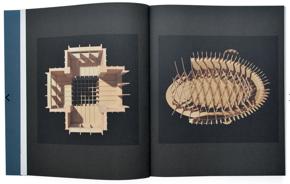 An open book or magazine spread showing two architectural model renderings on dark pages. The left page features a light wood-toned geometric structure with a central opening, and the right page shows a complex lattice-like oval structure in similar light wood tones against a black background.