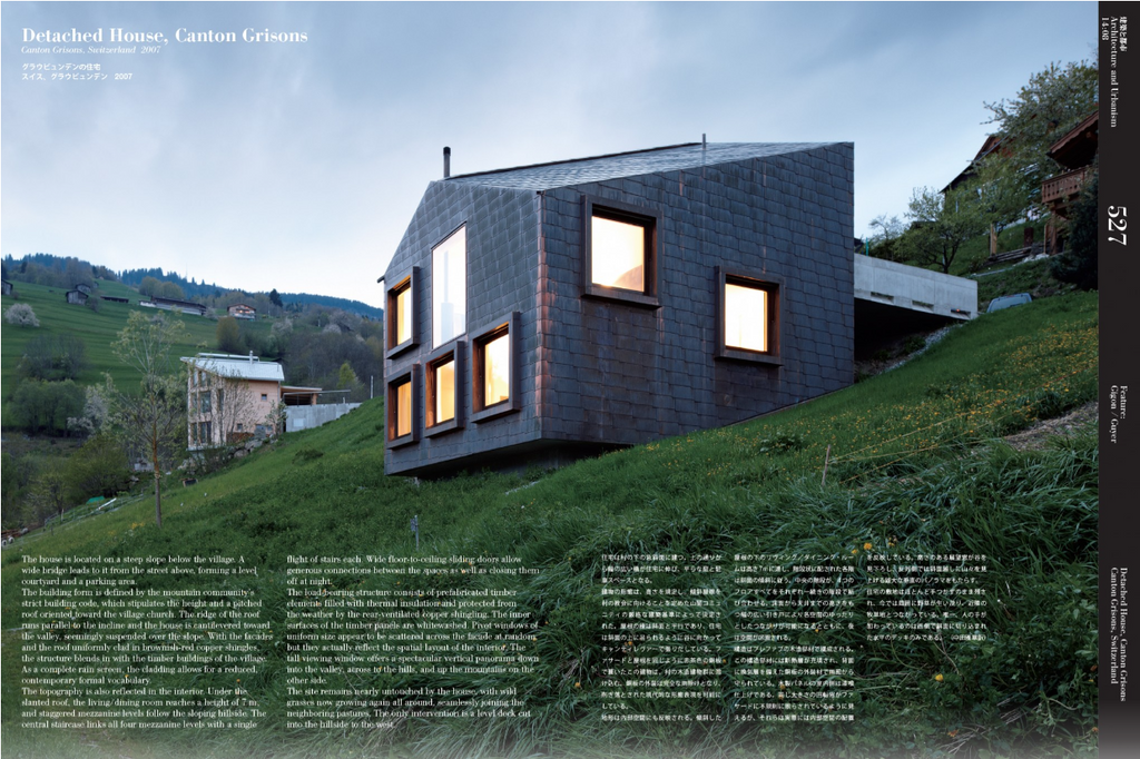 A magazine-style architectural photo print featuring the detached house Canton Grims in the Cantons Grims area, with a dark gray shingled exterior, glowing windows, and a grassy hillside background.
