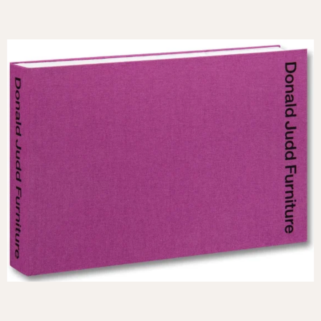 A hardcover book or publication titled 'Donald Judd Furniture' with a textured magenta-purple fabric cover, shown at an angle on a light gray background.