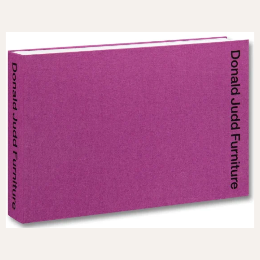 A hardcover book or publication titled 'Donald Judd Furniture' with a textured magenta-purple fabric cover, shown at an angle on a light gray background.
