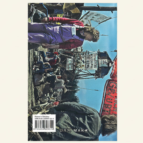 A printed  book cover photographed against a white background. The cover shows a street protest scene with people, signs, and a blue sky, plus the visible text 'DAMASK' and a barcode label near the bottom left.